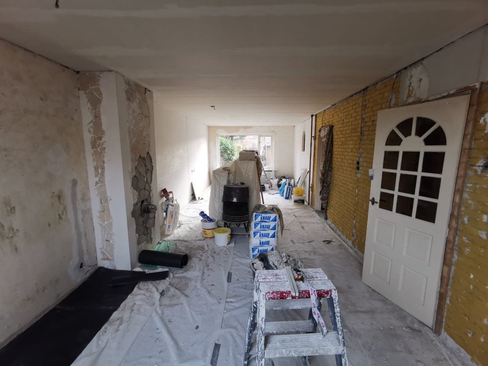 Woonkamer in een bestaande woning voor de renovatie: oud behang en pleisterwerk op de muren, gele bakstenen wand